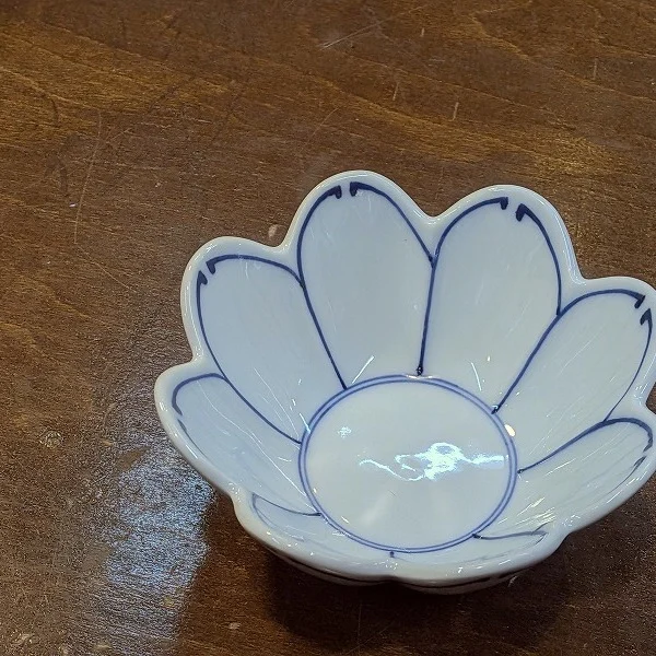 菊割線紋菊割小付

この小鉢は、花びらのような優しい形と、淡い藍の線が調和した上品な器です。食卓に置くだけで、まるで一輪の花が咲いたような華やかさを添えてくれます。
お浸しや香の物、和え物を少し盛るのにちょうどよい大きさで、料理を引き立てながらも主張しすぎない控えめな美しさがあります。
手に取ると軽やかで、縁のカーブもやわらかく、日常使いにもおもてなしにもぴったりです。
直径約9cm 深さ約3.5cm